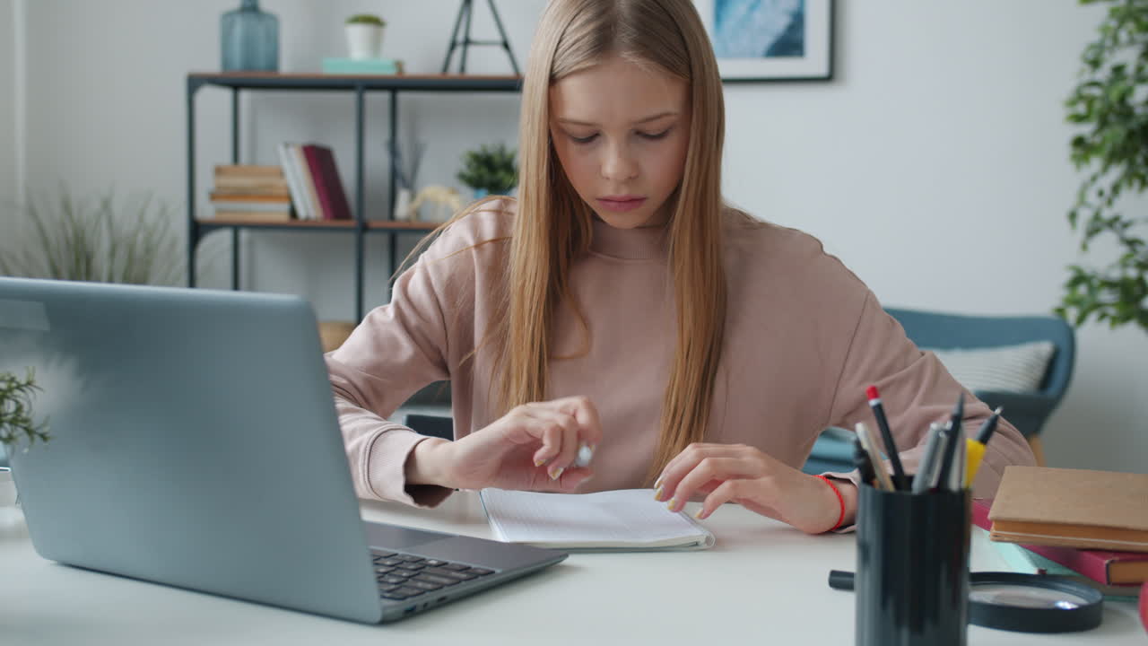 Teenage girl studying at home with laptop and notebook
