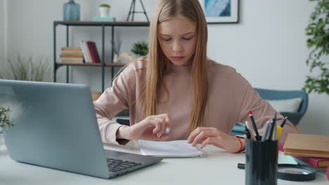 teenage girl studying at home with laptop and notebook