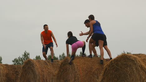 rear view of fit mixed-race friends helping a man while jumping from hay bales 4k