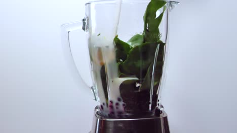 verter leche sobre espinacas, frutas y bayas, en una licuadora, mientras se hace un batido saludable - fondo gris - vista estática