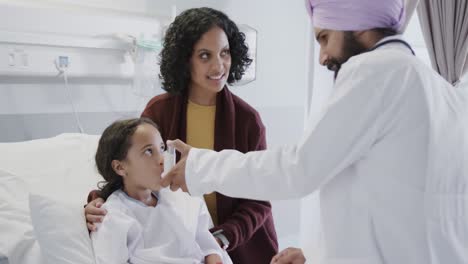 Happy-biracial-doctor-using-inhaler-on-sick-girl-patient-with-mother-in-hospital-in-slow-motion