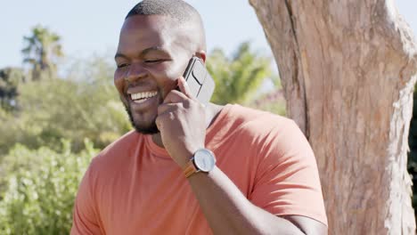 happy african american talking on smartphone in sunny garden, in slow motion