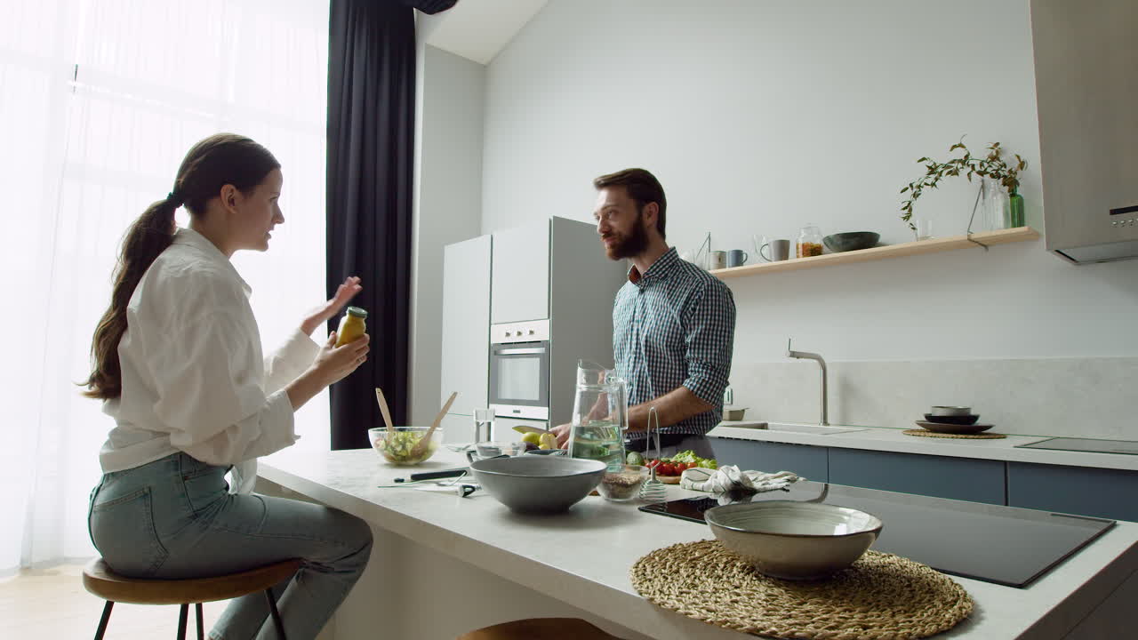 pareja alegre charlando y preparando una sabrosa ensalada en una cocina moderna