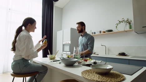 fröhliches paar, das in einer modernen küche plaudert und einen leckeren salat zubereitet