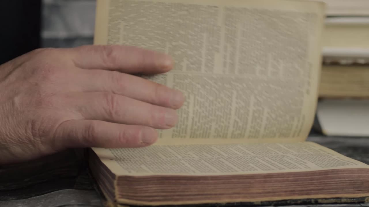 Inquadratura ravvicinata con carrellata di una mano che sfoglia le pagine di un vecchio libro
