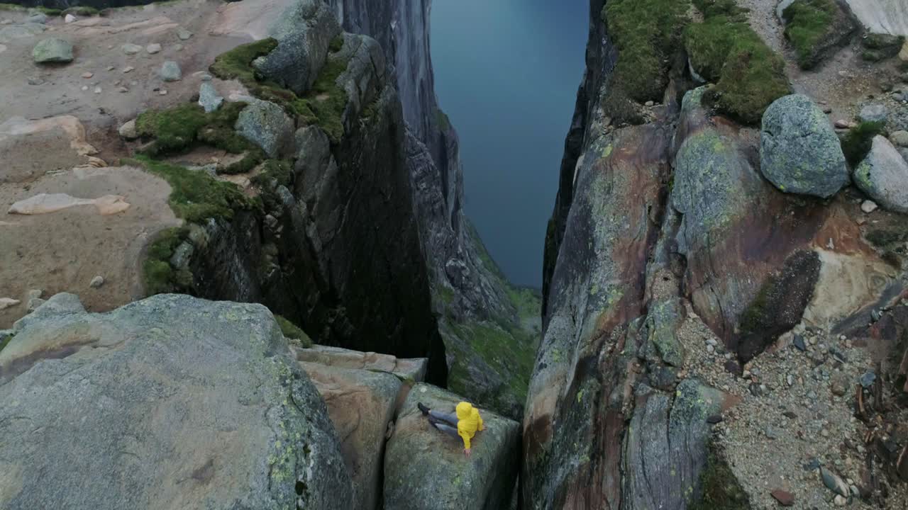 Solo traveler in yellow jacket balanced on boulder wedged between high cliffs