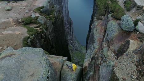 solo traveler in yellow jacket balanced on boulder wedged between high cliffs