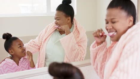 Happy-unaltered-african-american-mother-and-daughter-brushing-teeth-in-bathroom,-in-slow-motion