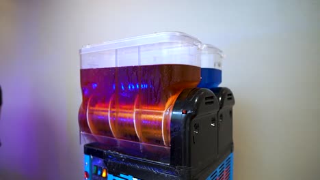 máquina fangosa que gira jarabe líquido rojo recién puesto para mezclarlo con una bebida congelada aislada con fondo blanco colocado en el interior para eventos para tratar a los invitados a cámara lenta