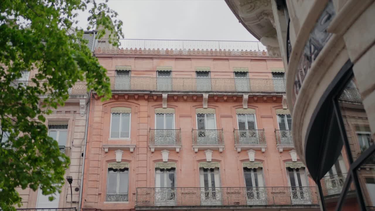 edificio de color rosa pastel con balcones ornamentados y follaje verde en toulouse, francia