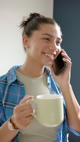 vertical video of smiling biracial teenage girl with tea talking on smartphone, slow motion