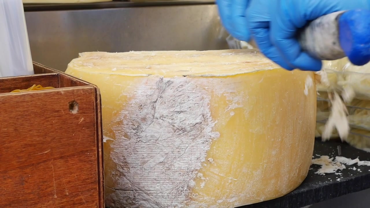 Chef che raschia la crosta da una grande forma di formaggio stagionato