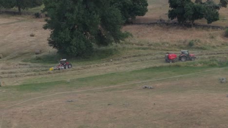 167mm slow motion drone footage of two farm tractors harvesting in a meadow one makes rows of hay and another bales them and makes them round there are storks looking for food in the meadow