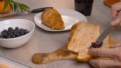 un hombre pone mermelada de arándanos en croissants con un cuchillo en una tabla de cortar de madera.