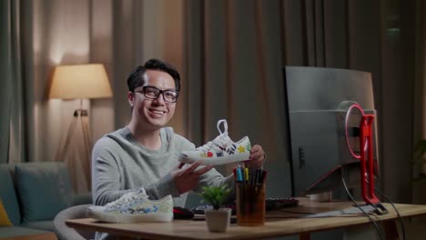 diseñador de calzado masculino asiático sonriendo a la cámara mientras trabaja en una computadora de escritorio en casa