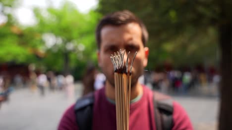 tourist holding incense sticks at beijing's lama temple, with people and greenery in background