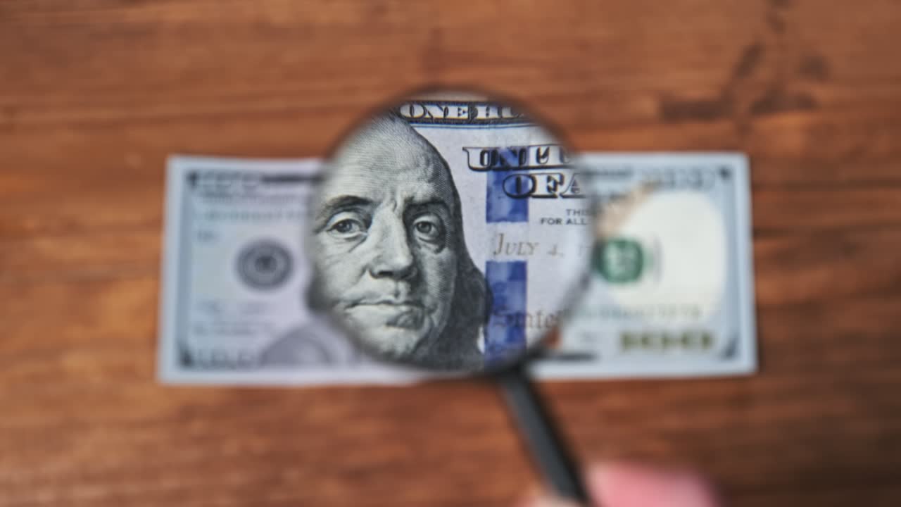 Sadan dollarin seteliä tarkastellaan suurennuslasilla puupöydällä.