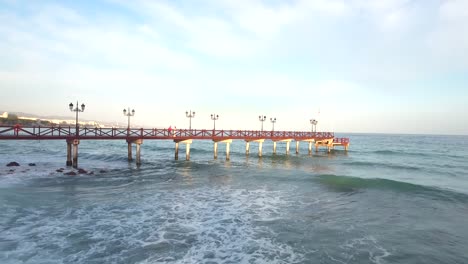 wooden-pier-in-the-sea-with-waves-rolling-in,-romantic-at-sunset-shot-filmed-in-marbella,-malaga,-spain