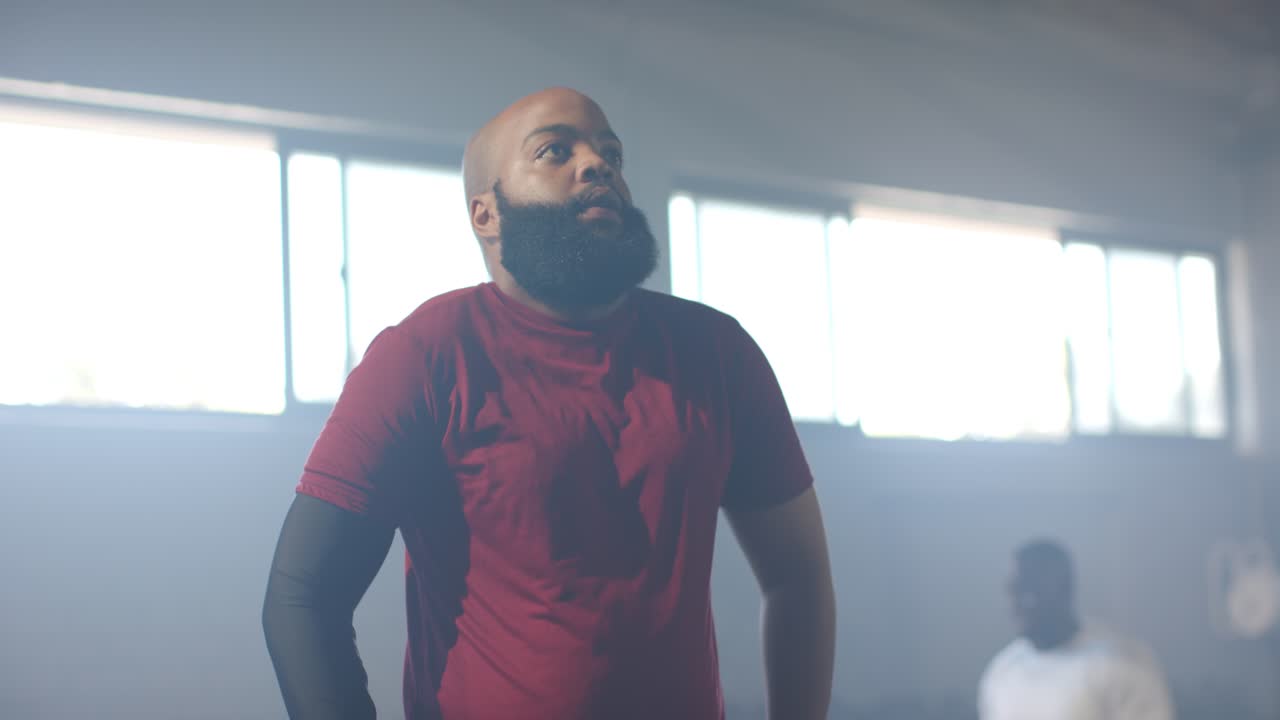 Afrikanske mænd ser på en mand i rød T-shirt med sorte ærmer, der trækker vejret dybt før træning i et fitnesscenter.
