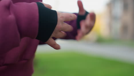 workout expert in hoodie presses palms together and flexes fingers with purposeful focus in gentle warmup to reduce tension before outdoor fitness session under open sky at urban park near apartments