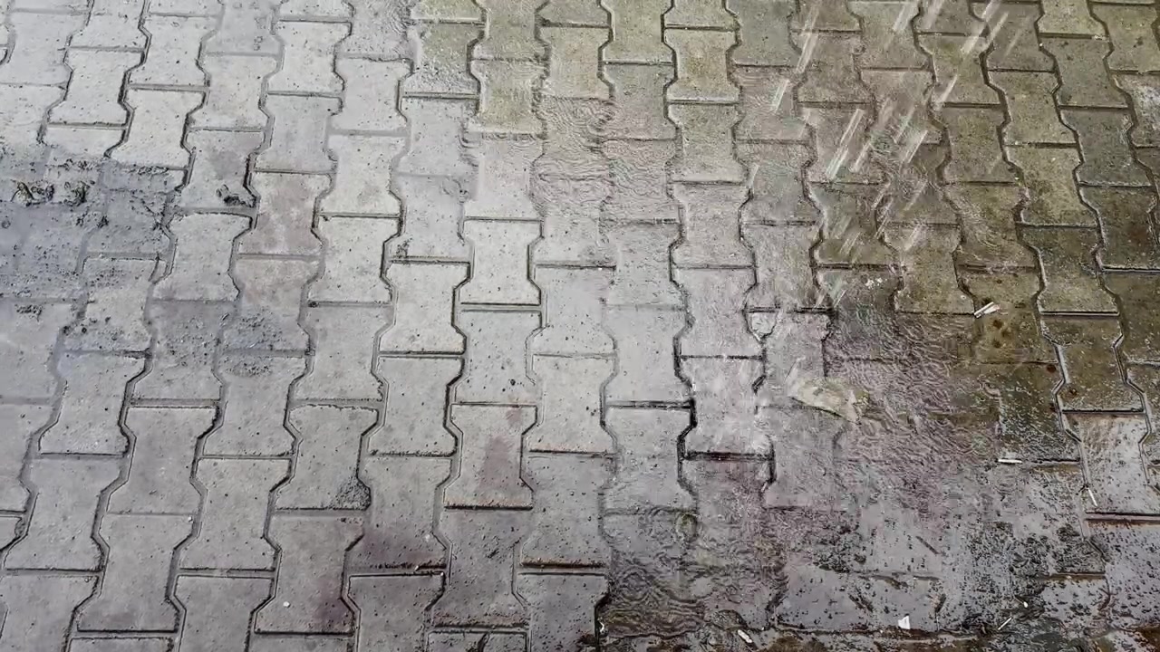 Water falling from a roof onto wet interlocking brick pavement creating ripples and splashes during heavy monsoon weather