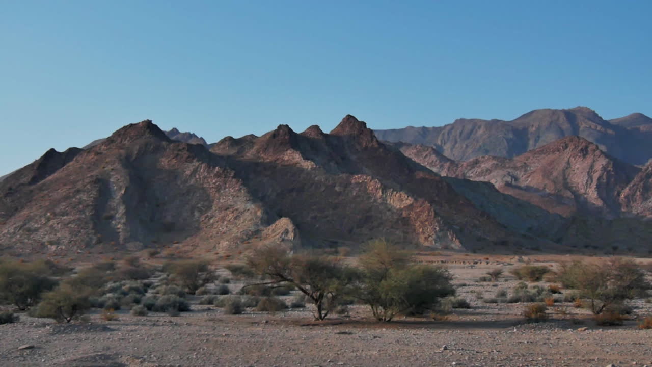 Rugged dry hills and sharp peaks of the Omani desert landscape lit by the afternoon sun travelling side from car