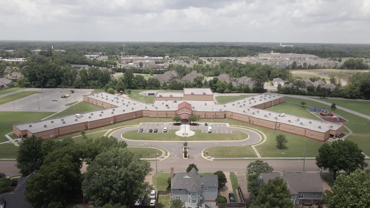 A drone zoom-in shot capturing a suburban neighborhood in the United States, showcasing tree-lined streets and residential houses. The greenery and -planned layout highlight the peaceful.