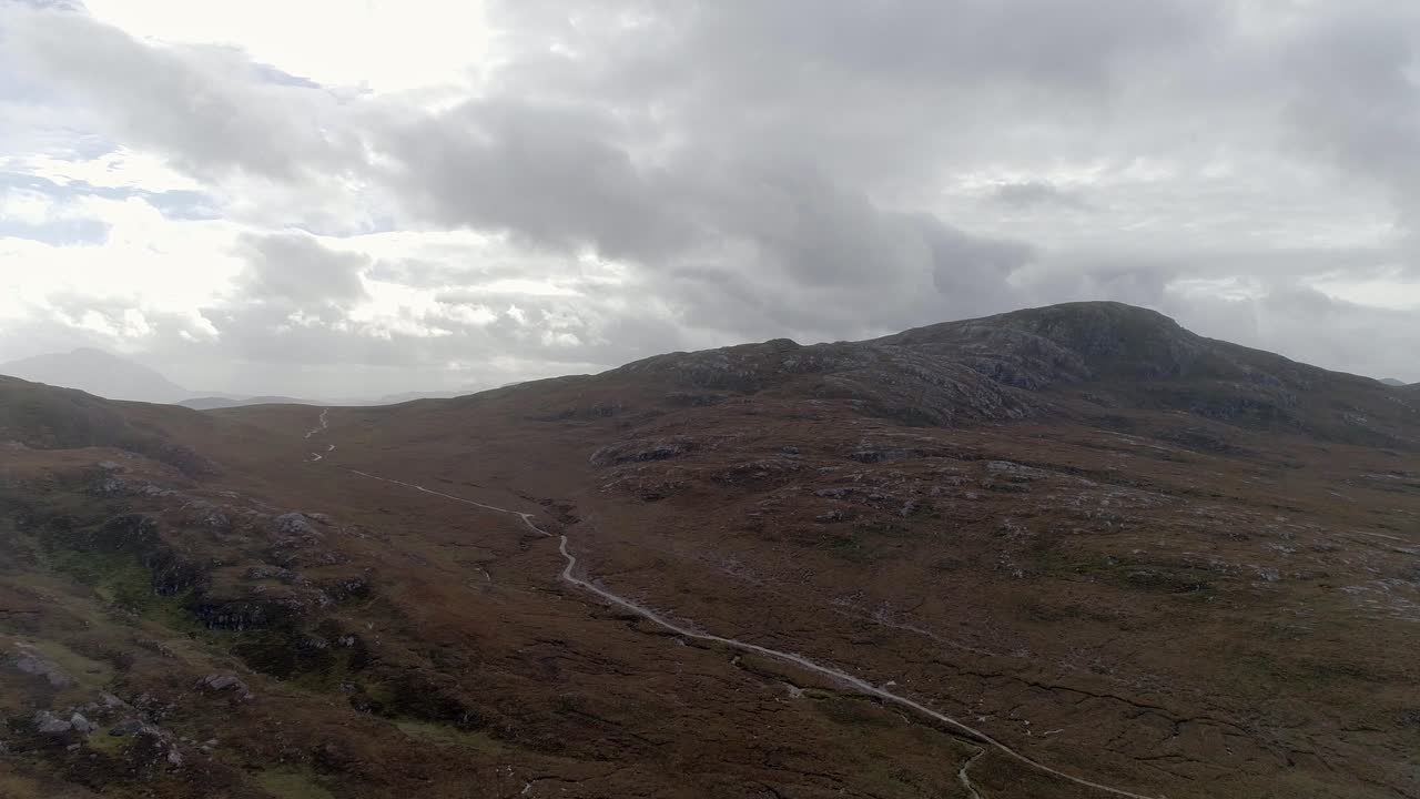 amplio seguimiento aéreo hacia adelante hacia una escena montañosa en las tierras altas escocesas con un sendero que corta directamente a través de dos picos
