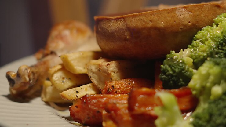 Vista laterale di un tradizionale arrosto festivo di pollo intero in stile inglese, con carote arrosto, pastinaca con broccoli al vapore e Yorkshire pudding