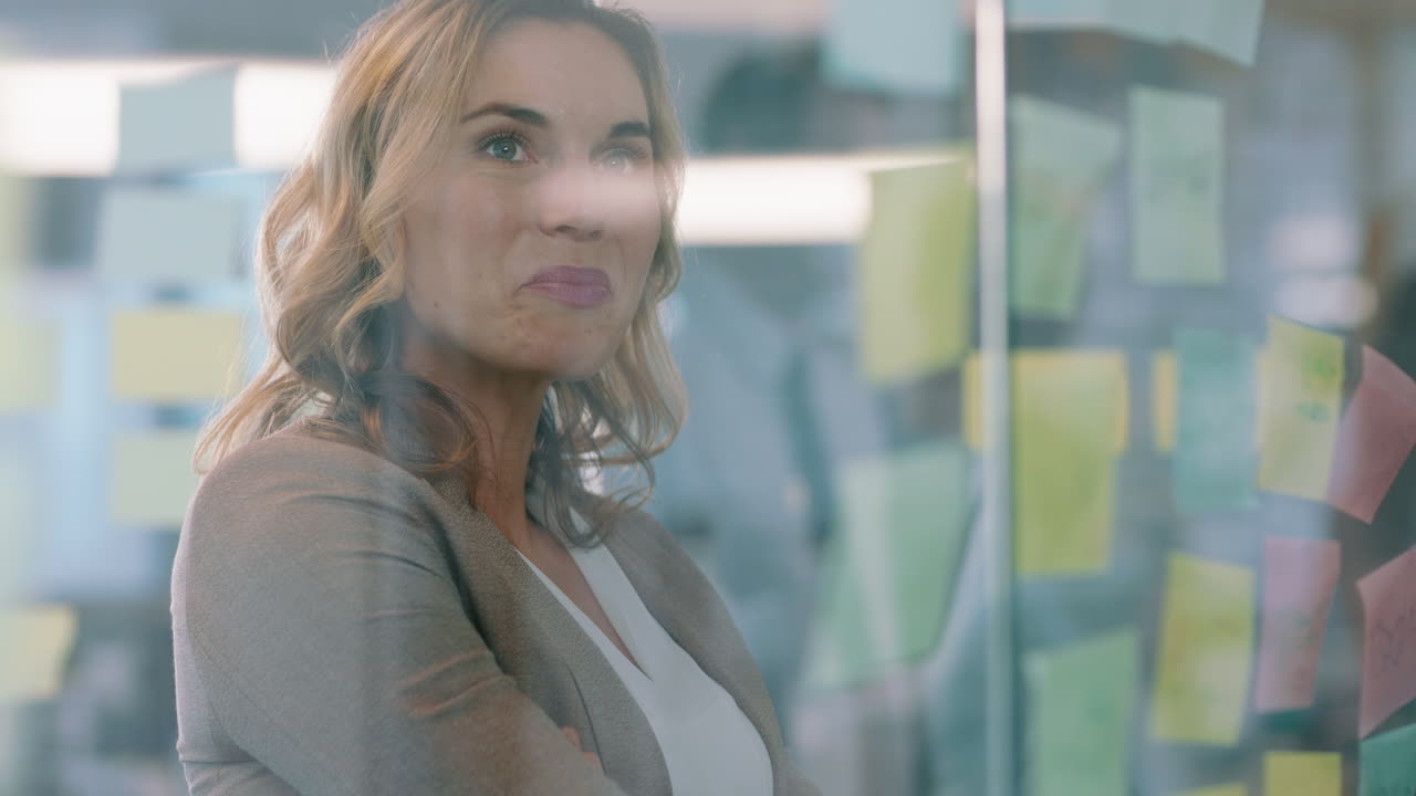 hermosa mujer de negocios usando notas adhesivas haciendo una lluvia de ideas en una pizarra de vidrio sonriendo orgullosa de la solución exitosa planeando estrategia resolviendo problemas con un mapa mental creativo en la oficina 4k