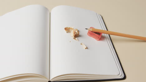 primer plano de un cuaderno abierto con lápiz y afilador de lápiz en fondo beige, en cámara lenta