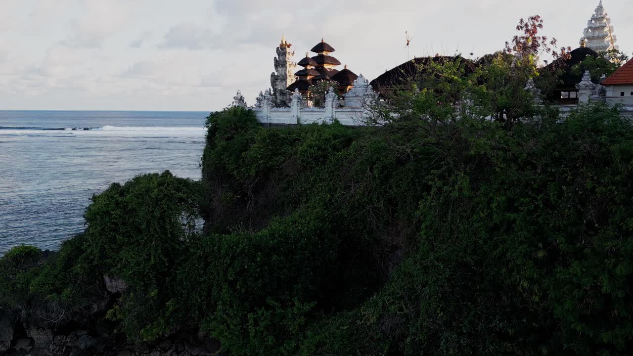 Beautiful aerial view of a traditional Balinese temple standing above Uluwatu’s cliffs. The ocean breeze and golden light enhance the serene, cultural atmosphere of this coastal sanctuary