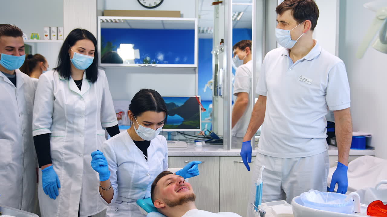 Practical lesson for students of orthodontic department. Female student sits near the patient and teacher speaks at backdrop.