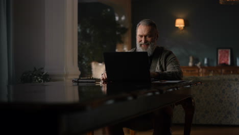 Joyful-old-man-making-video-call-on-computer-in-luxury-cabinet.-Happy-senior-man