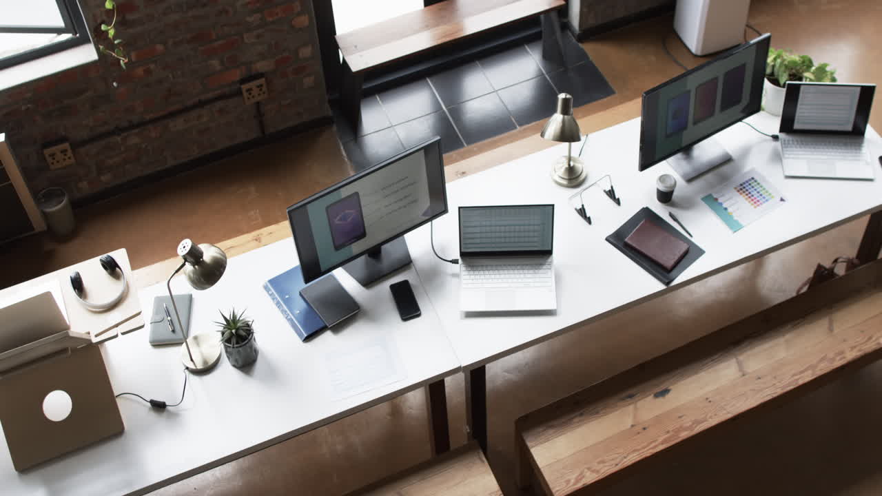 Multiple workstations with laptops, smartphones, and desk lamps in a business setting
