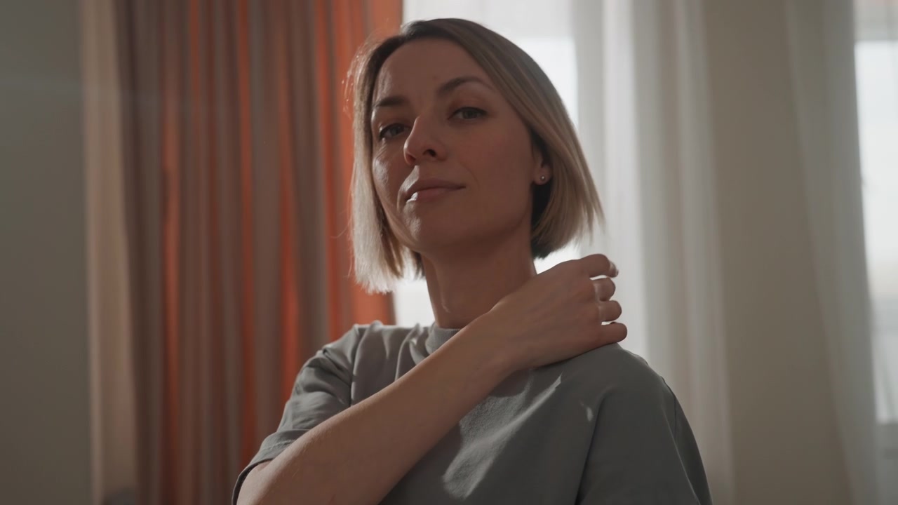 Donna bianca che si sistema la collana vicino alla finestra con un bagliore laterale di luce e tende calde, espressione contemplativa, gesti delicati delle mani, che prepara la voce e idee per canzoni, atmosfera da studio in camera da letto, morbida.