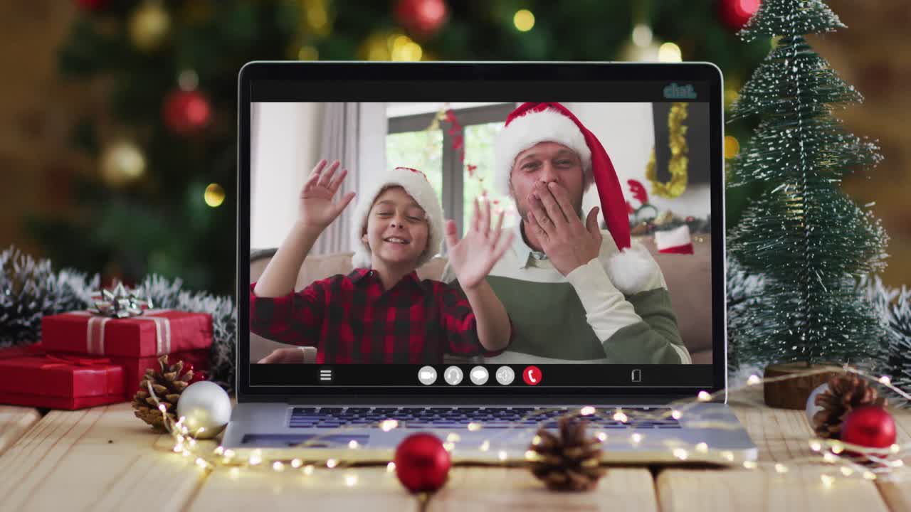 padre y hijo felices saludando en una videollamada en una computadora portátil, con decoraciones de navidad y árbol