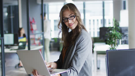 Porträt-Einer-Kaukasischen-Geschäftsfrau,-Die-Im-Büro-Mit-Laptop-Steht-Und-In-Die-Kamera-Blickt-Und-Lächelt