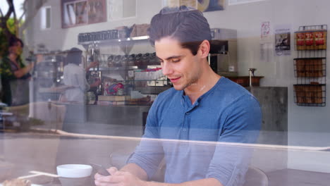 joven cliente masculino comprobando su teléfono inteligente en una cafetería