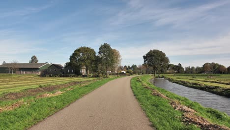 Left-to-right-pan-shot-of-green-and-lush-fields-of-hay-that-has-been-harvested-next-to-a-small-road-and-a-river-during-a-windy-day-in-the-Netherlands