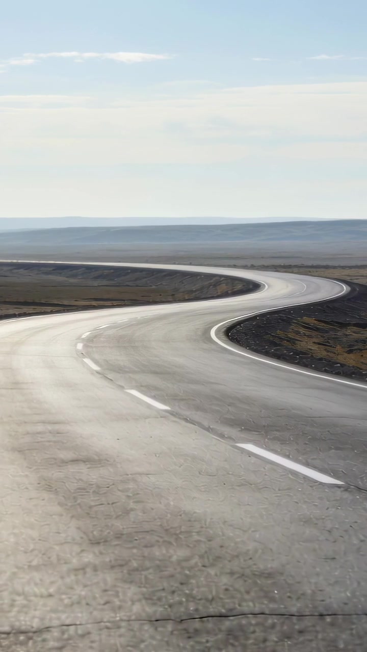 Vertical video: Frames showing winding paved road on plain drawing eye toward hills, dashed lanes