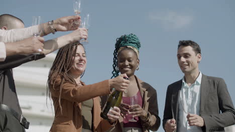 front view of happy woman opening champagne with coworkers