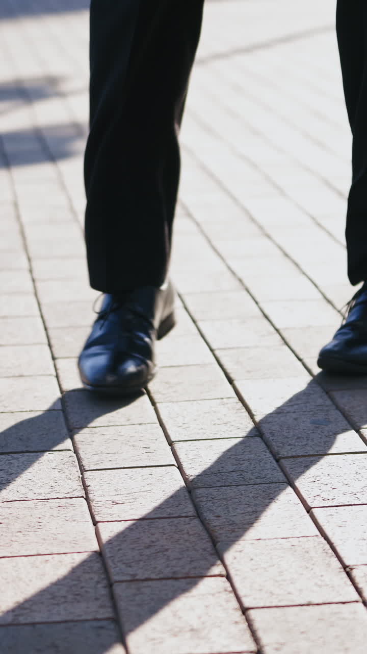Close-up for legs of man in black shoes dancing in the street. Male's feet in black shoes and trousers dances happily on the pavement outdoors. Vertical video