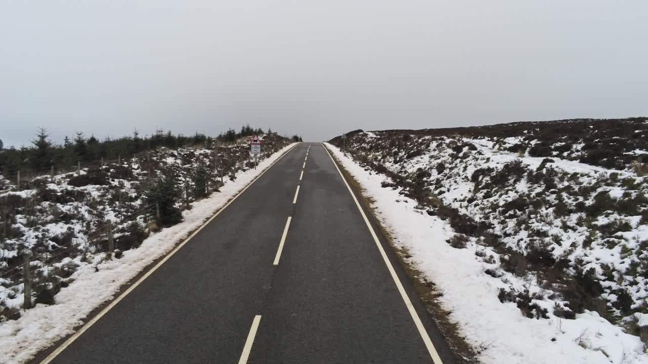 고지대의 눈 덮인 시골 황무지를 가로질러 먼 거리로 날아가는 긴 도로