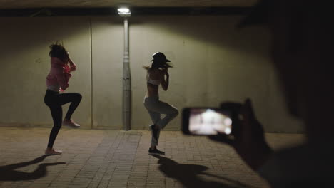 bailarina feliz bailarina de hip hop chicas bailando bajo la luz de la calle amigo usando teléfono inteligente tomando video disfrutando de compartir en las redes sociales en la ciudad por la noche