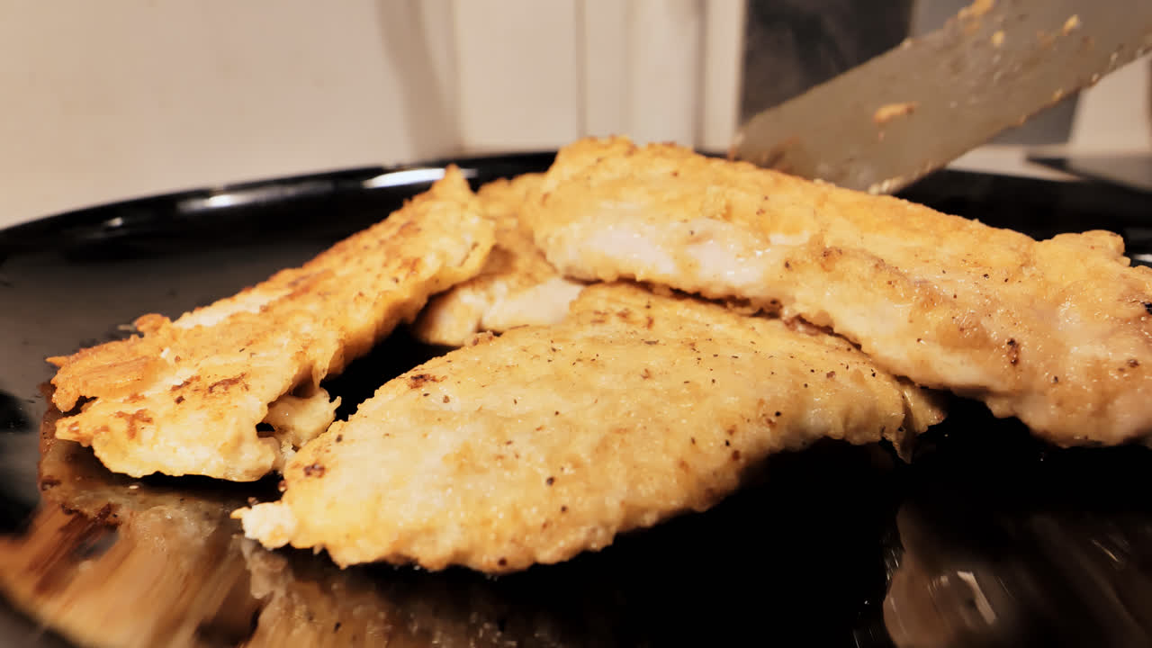 Juicy breaded chicken cutlets being served fresh from pan to black plate at home