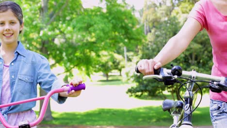 cute mother and daughter pushing their bikes together in the park