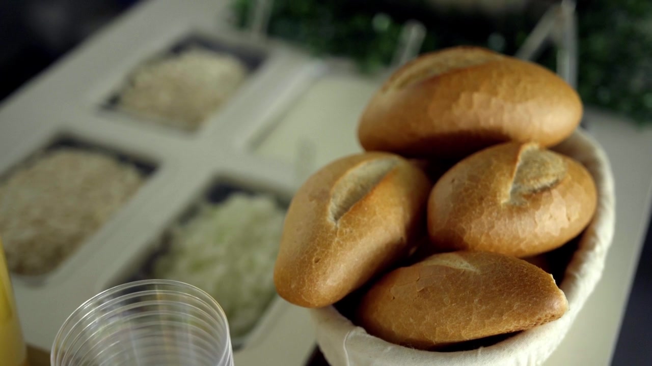 Fresh bread rolls arranged in basket on catering counter with buffet food background, dining setup and hospitality service atmosphere indoors