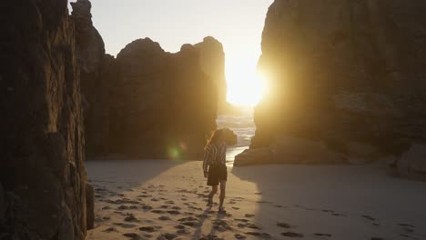 woman walking on a beach at sunset between rocks