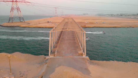 two jet skis speed under decrepit bridge in armageddon setting surrounded by electic pylons, drone aerial